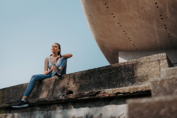 Young fitness woman resting after workout session in the city. Beautiful sporty woman enjoying sunrise after morning excercise.