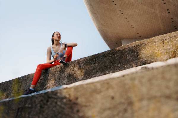 Young fitness woman in sportswear resting after hard workout session in the city. Sporty woman catching breath and drinking water after morning excercise.