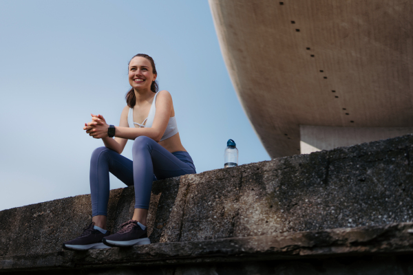 Young fitness woman in sportswear resting after workout session in the city. Beautiful sporty woman enjoying sunrise after morning excercise.