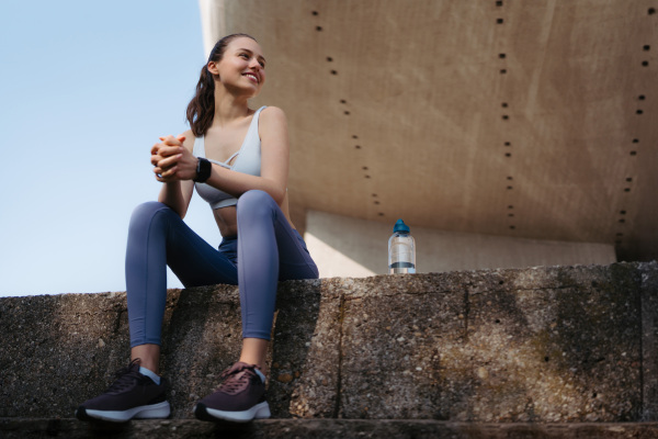 Young fitness woman in sportswear resting after workout session in the city. Beautiful sporty woman enjoying sunrise after morning excercise.