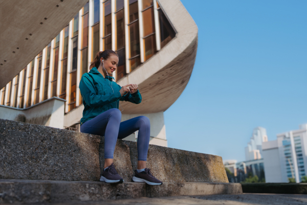 Side view of sporty woman checking her performance on smartwach after workout session. Woman using smartwatch to sending text message, calling.