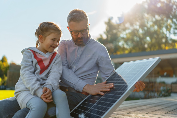 Father showing his little daughter solar photovoltaics panels, explaining how it working. Alternative energy, saving resources and sustainable lifestyle concept.