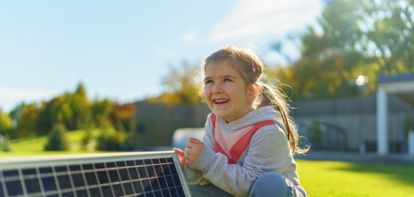 Little girl holding a photovoltaics solar panel. Alternative energy, saving resources and sustainable lifestyle concept.