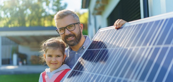 Father with his little daughter near the house with solar panels. Alternative energy, saving resources and sustainable lifestyle concept.