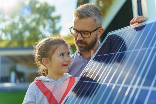 Father with his little daughter near the house with solar panels. Alternative energy, saving resources and sustainable lifestyle concept.