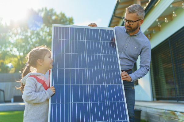 Father with his little daughter near the house with solar panels. Alternative energy, saving resources and sustainable lifestyle concept.