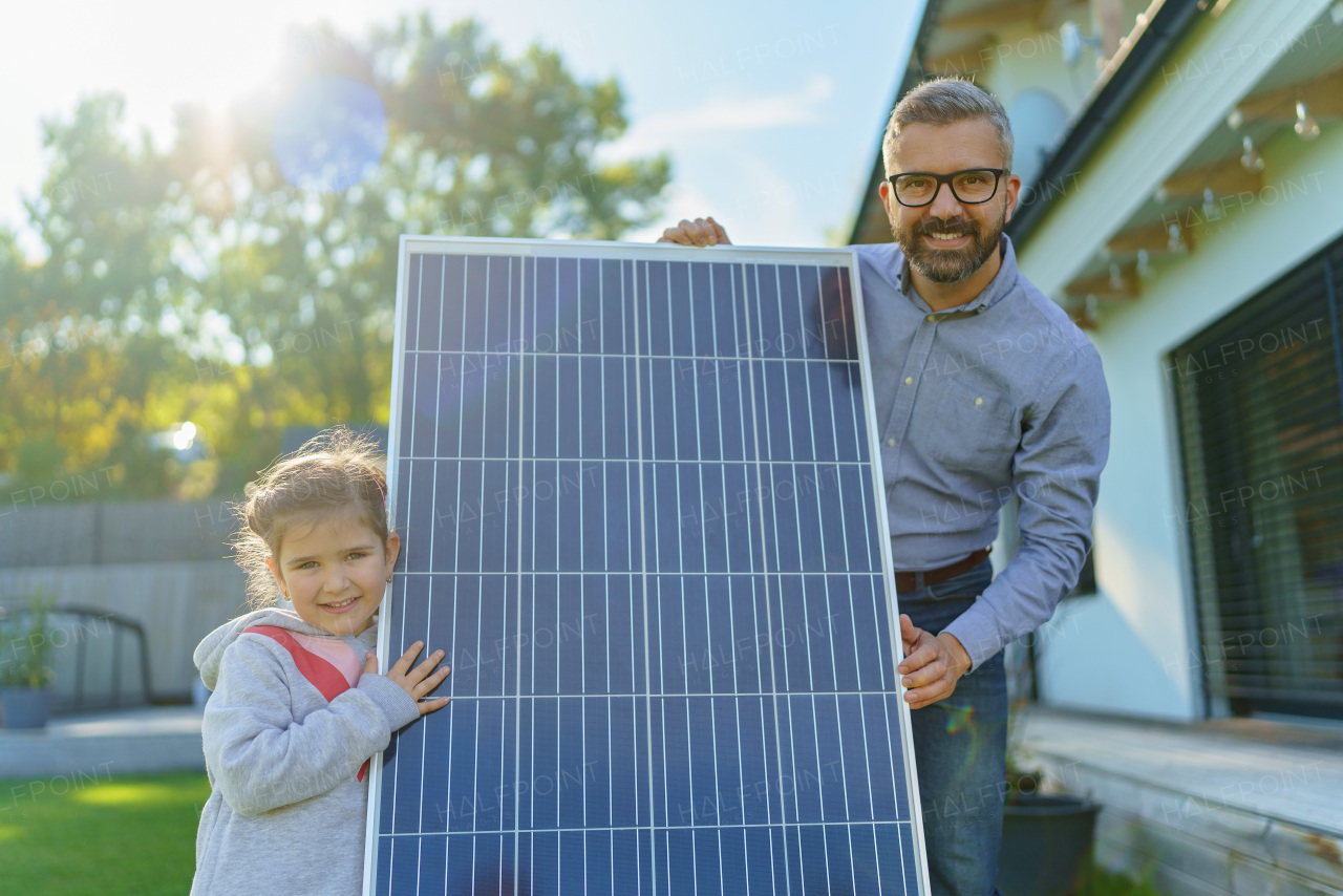 Father with his little daughter near the house with solar panels. Alternative energy, saving resources and sustainable lifestyle concept.