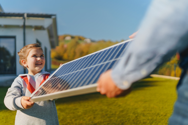 Father with his little daughter catching sun at solar panel,charging at the backyard. Alternative energy, saving resources and sustainable lifestyle concept.