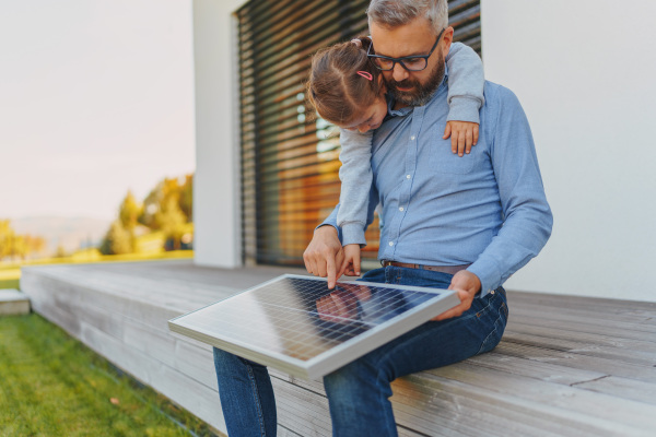 Father showing his little daughter a solar photovoltaics panels, explaining how it works. Alternative energy, saving resources and sustainable lifestyle concept.