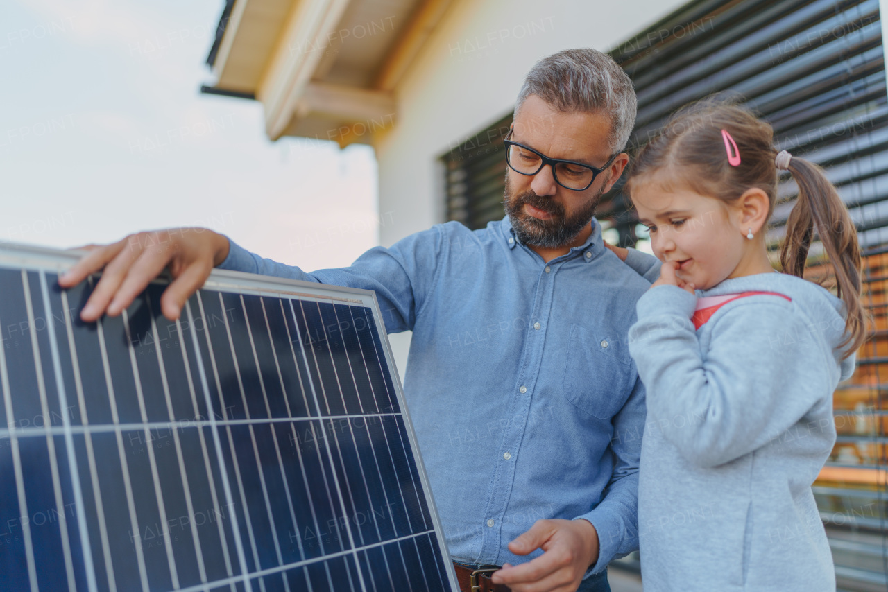 Father showing his little daughter solar photovoltaics panels, explaining how it working. Alternative energy, saving resources and sustainable lifestyle concept.