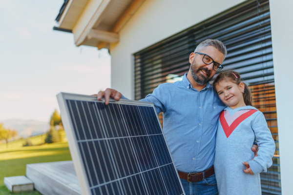 Father with his little daughter near the house with solar panels. Alternative energy, saving resources and sustainable lifestyle concept.