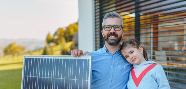 Father with his little daughter near the house with solar panels. Alternative energy, saving resources and sustainable lifestyle concept.