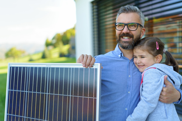 Father with his little daughter near the house with solar panels. Alternative energy, saving resources and sustainable lifestyle concept.