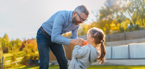 Father with his little daughter having fun in their backyard during a sunny autumn day.