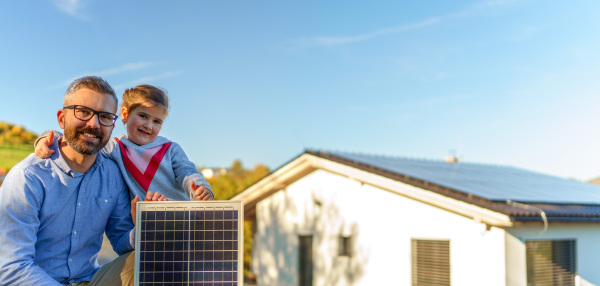 Father with his little daughter near the house with solar panels. Alternative energy, saving resources and sustainable lifestyle concept.