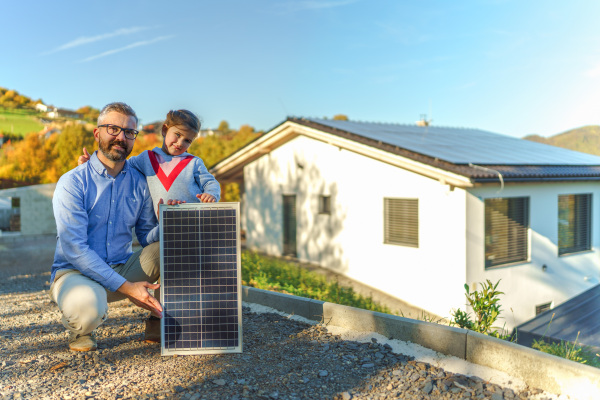 Father with his little daughter near the house with solar panels. Alternative energy, saving resources and sustainable lifestyle concept.