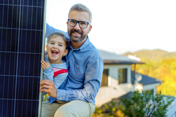 Father with his little daughter near the house with solar panels. Alternative energy, saving resources and sustainable lifestyle concept.