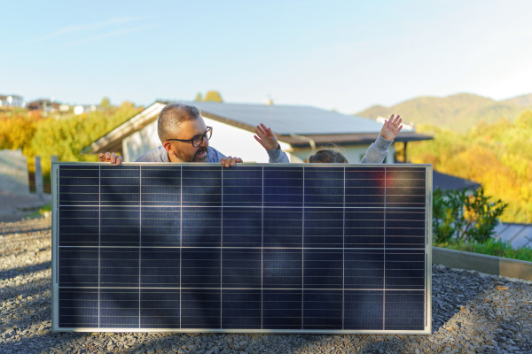 Father with his little daughter near the house with solar panels. Alternative energy, saving resources and sustainable lifestyle concept.