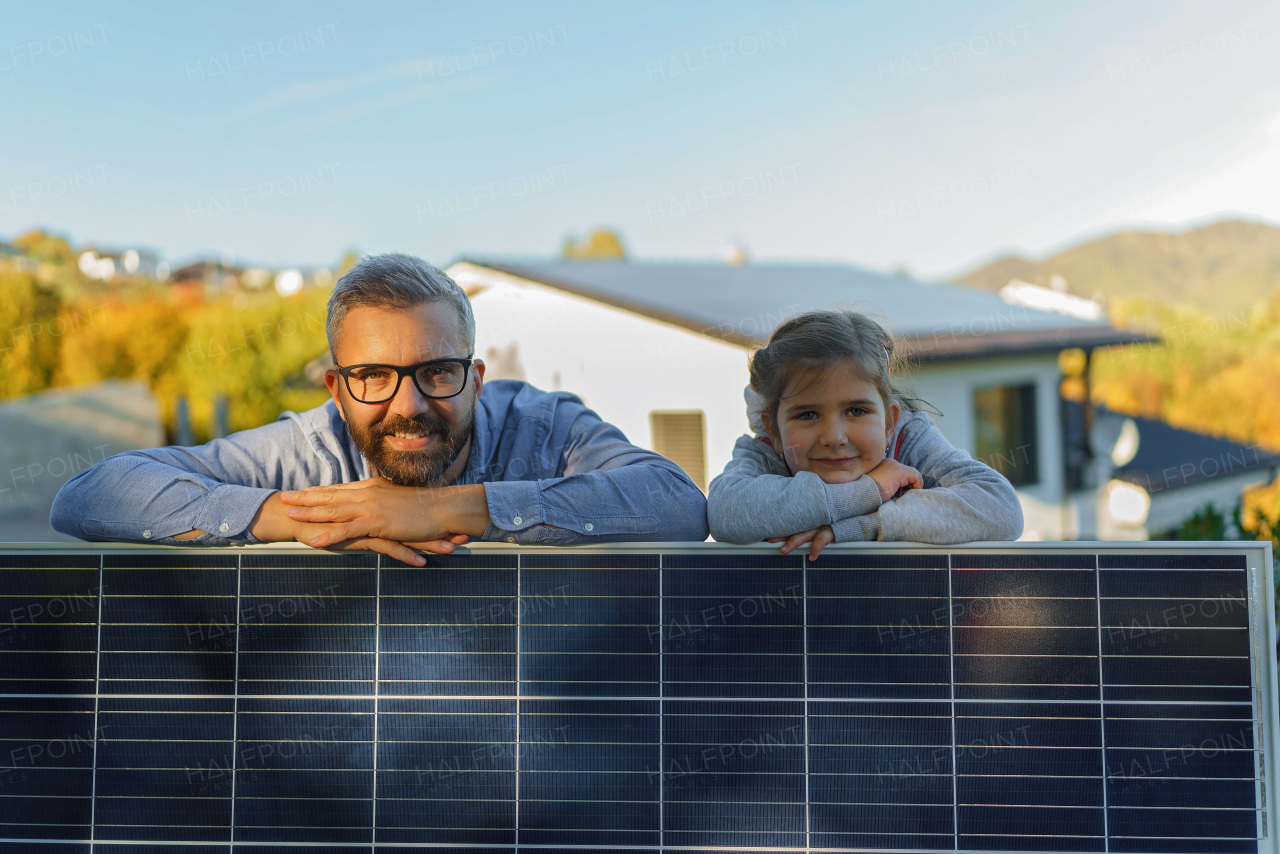 Father with his little daughter near the house with solar panels. Alternative energy, saving resources and sustainable lifestyle concept.