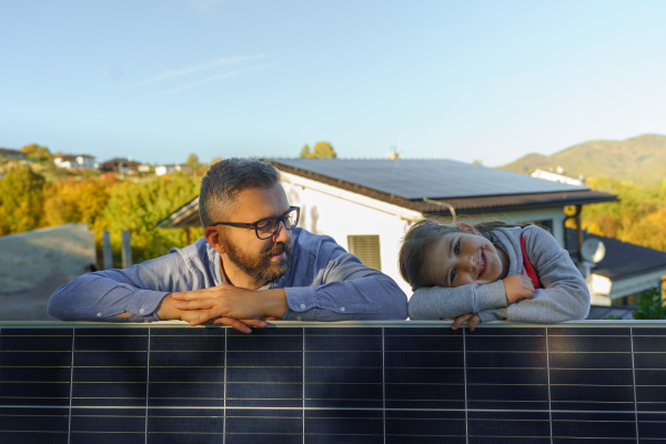 Father with his little daughter near the house with solar panels. Alternative energy, saving resources and sustainable lifestyle concept.