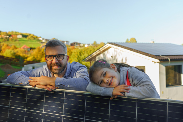 Father with his little daughter near the house with solar panels. Alternative energy, saving resources and sustainable lifestyle concept.