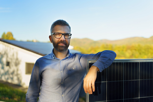 Businessman holding a solar panel, standing outdoor at a garden.