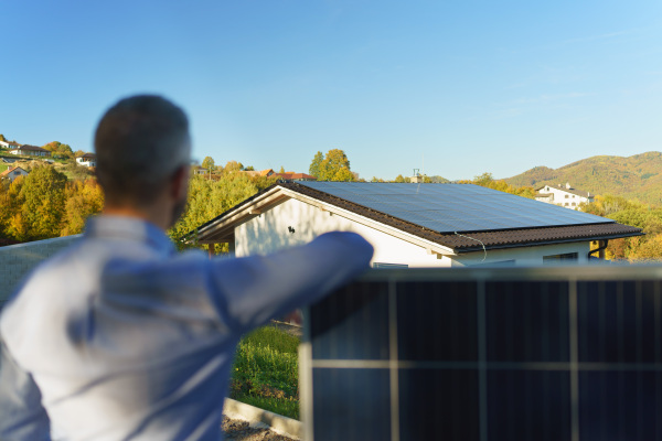 Businessman holding a solar panel, standing outdoor at a garden.