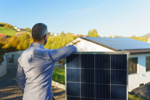 Businessman holding a solar panel, standing outdoor at a garden.