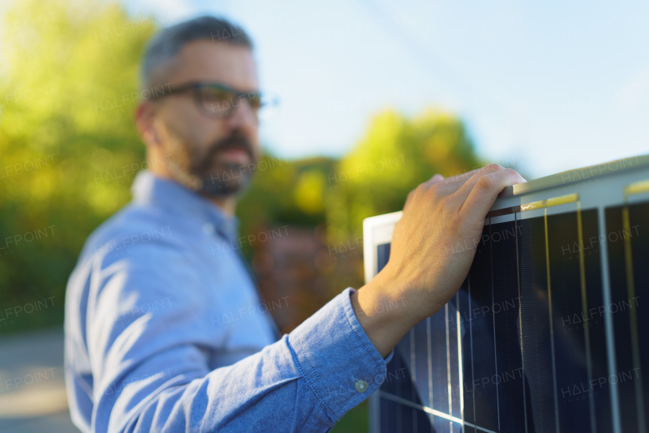 Businessman holding solar panel, standing outdoor at a garden.