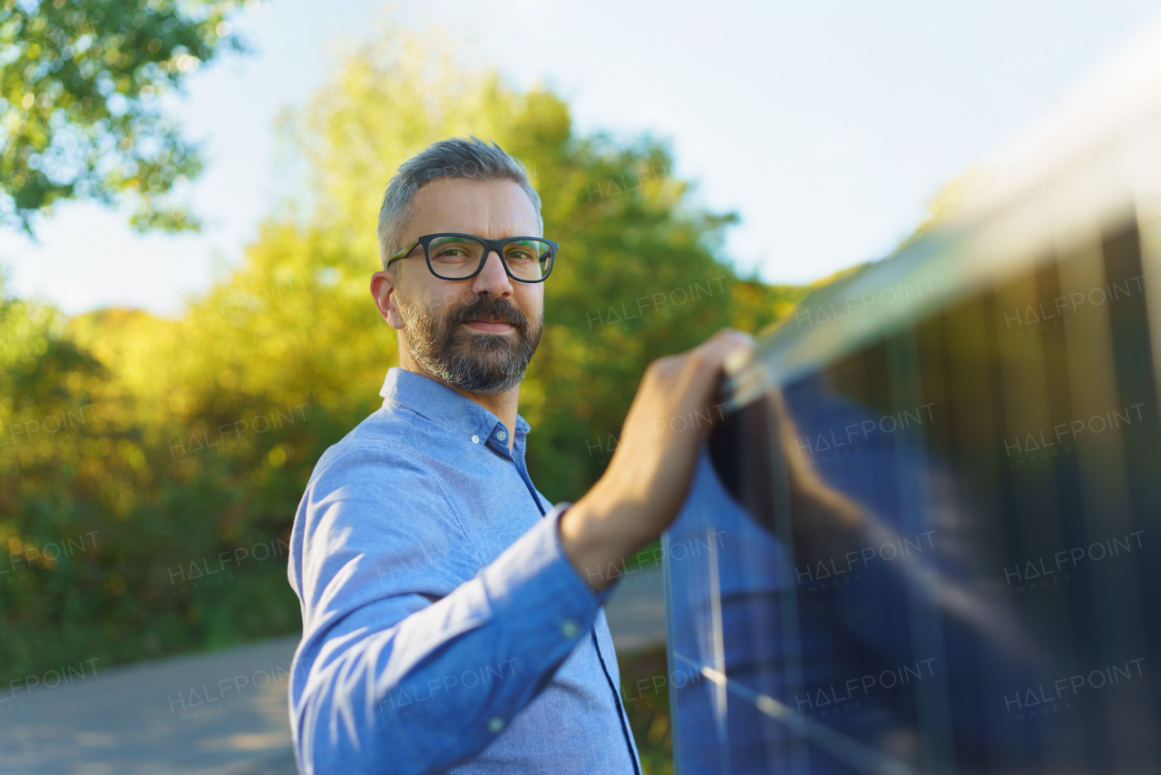 Businessman holding solar panel, standing outdoor at a garden.