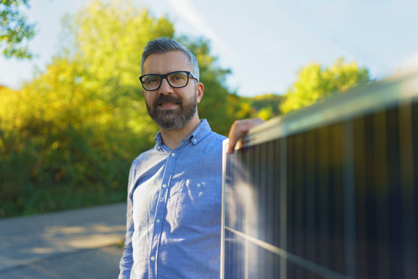 Businessman holding solar panel, standing outdoor at a garden.