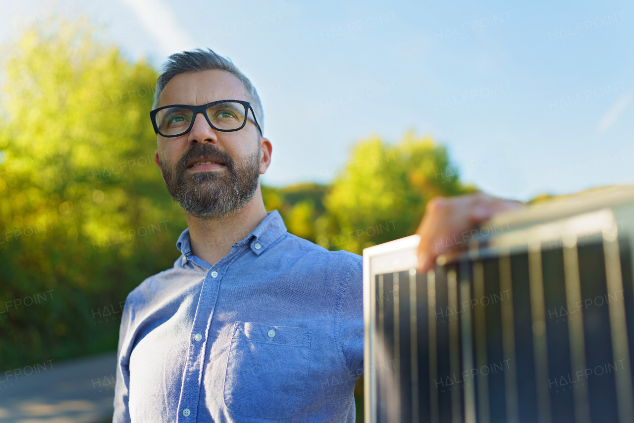 Businessman holding solar panel, standing outdoor at a garden.