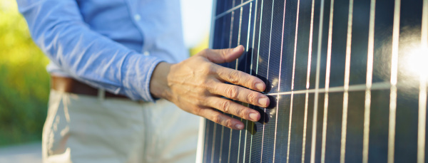 Close-up of businessman holding solar panel, standing outdoor at a garden.