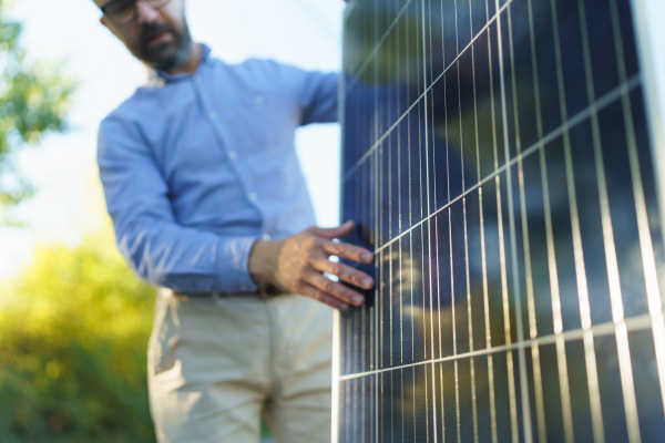 Businessman holding solar panel, standing outdoor at a garden.