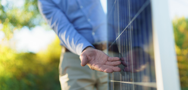 Mid section of businessman holding solar panel, standing outdoor at a garden.