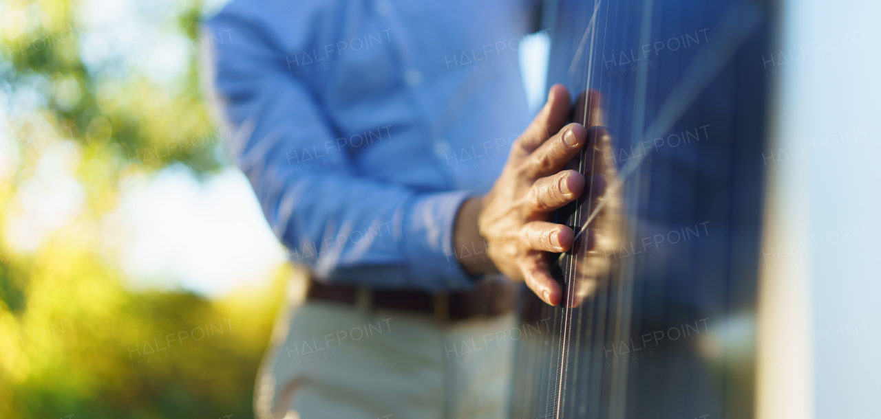 Close-up of businessman holding solar panel, standing outdoor at a garden.