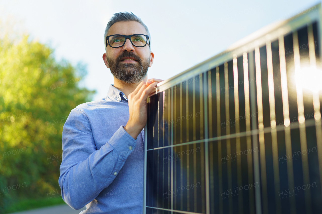 Businessman holding solar panel, standing outdoor at a garden.