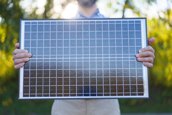 Close-up of businessman holding solar panel, standing outdoor at a garden.