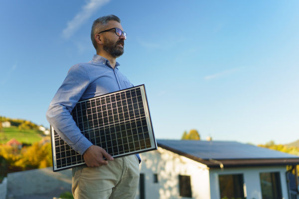 Businessman holding solar panel, standing outdoor at a garden.