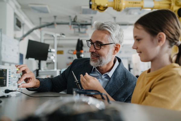 Father and girl during take your daughter to work day, encouraging girl in career in robotics. Teacher showing young schoolgirl how to assemble small robot.