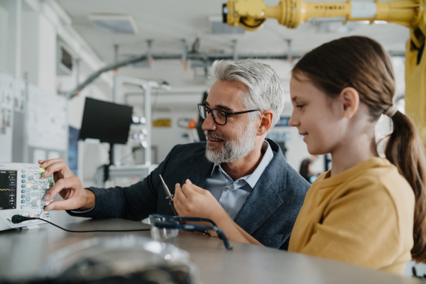 Father and girl during take your daughter to work day, encouraging girl in career in robotics. Teacher showing young schoolgirl how to assemble small robot.