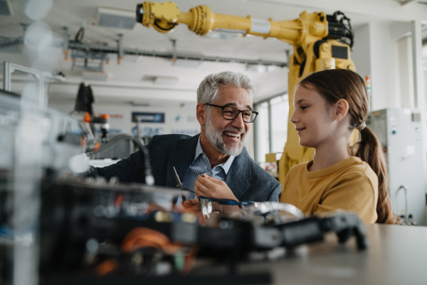 Father and girl during Kid at work day, encouraging girl in career in robotics. Teacher showing young schoolgirl how to assemble small robot.