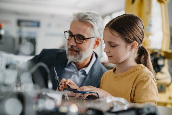 Father and girl during Kid at work day, encouraging girl in career in robotics. Teacher showing young schoolgirl how to assemble small robot.