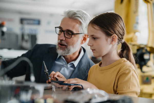 Father and girl during Kid at work day, encouraging girl in career in robotics. Teacher showing young schoolgirl how to assemble small robot.