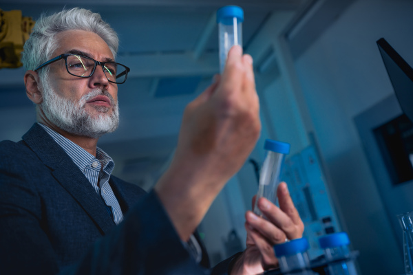 Male scientist in the laboratory holding test tube and intently looking at its contents.