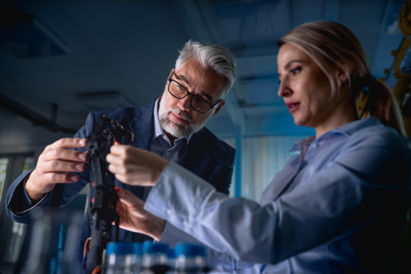 Two robotics engineers working on new project, standing in laboratory. Concept of modern technology in industries, automated processes, automotive.