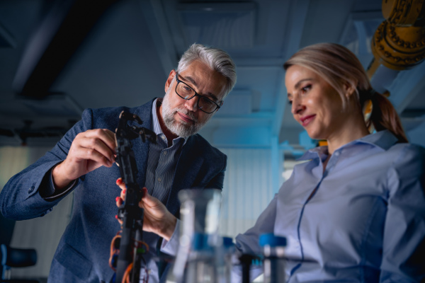 Two robotics engineers working on new project, standing in laboratory. Concept of modern technology in industries, automated processes, automotive.