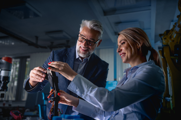 Two robotics engineers working on new project, calibring robotic prosthetic hand. Concept of modern technology in industries, automated processes, automotive.