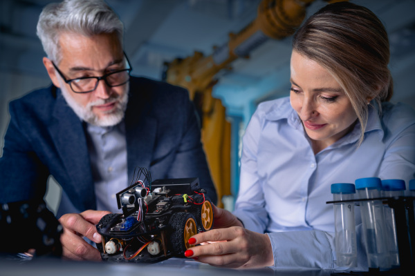 Two robotics engineers working on new project, standing in laboratory. Concept of modern technology in industries, automated processes, automotive.