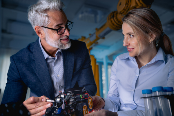 Two robotics engineers working on new project, standing in laboratory. Concept of modern technology in industries, automated processes, automotive.